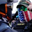 A member of a group wearing tactical gear and a patterned mask, engaged in a discussion with another individual, during a protest event. A member of a group wearing tactical gear and a patterned mask, engaged in a discussion with another individual, during a protest event.