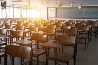 Empty classroom with wooden desks and chairs, sunlight streaming in from the windows.