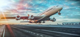 An airplane taking off from an airport runway with a colorful sky in the background.