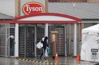 Entrance of a Tyson Foods plant with a person walking through the gates during rainy weather.
