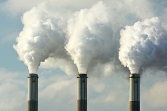 Smoke billowing from industrial chimneys against a cloudy blue sky.