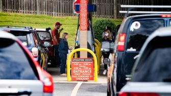 Cars lined up at a gas station with people refueling after the Colonial Pipeline cyberattack, indicating fuel shortages.