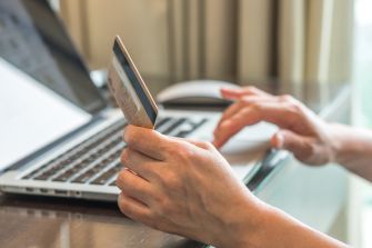 A person's hand holding a credit card while using a laptop.