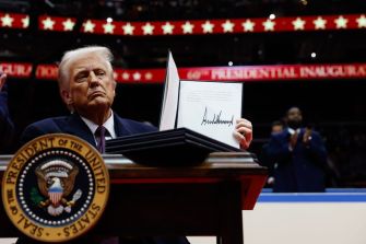 Donald Trump holding a signed executive order at a podium adorned with the presidential seal during an event.