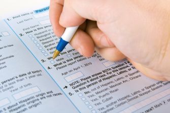 A close-up of a hand writing on a U.S. census form with checkboxes and demographic questions.