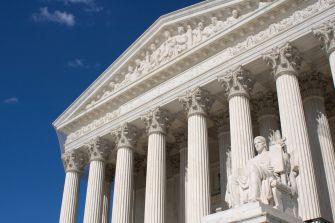 Image of the United States Supreme Court building, showcasing its neoclassical architecture and large columns against a blue sky.
