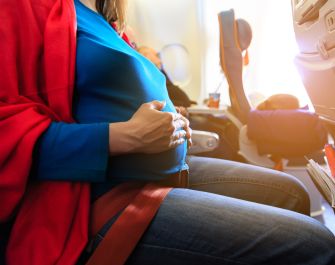 Pregnant woman seated on an airplane, showing a focus on her belly while wearing casual attire.