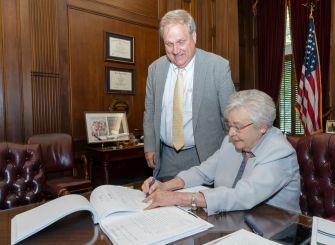 Governor Kay Ivey signing the Senate Bill 46 to legalize medical marijuana in Alabama, with a legislative advisor present.