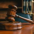 Gavel on a wooden court table with a backdrop of legal books and scales of justice. Gavel on a wooden court table with a backdrop of legal books and scales of justice.