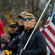 A group of people at a rally holding flags, with one person wearing a mask resembling a former president. A group of people at a rally holding flags, with one person wearing a mask resembling a former president.