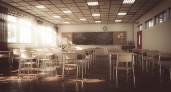 An empty classroom with desks facing a chalkboard, illuminated by natural light.