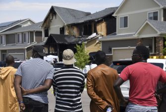 A group of individuals watching the aftermath of a house fire in a suburban neighborhood.