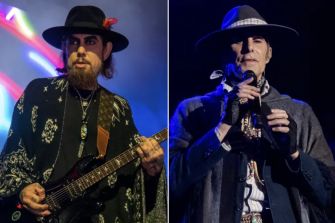 Two musicians performing on stage, one playing guitar and the other using a microphone with a tablet.