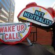 A person setting up a large sign that reads "WAKE UP CALL" and "NET NEUTRALITY" at a protest or rally. A person setting up a large sign that reads "WAKE UP CALL" and "NET NEUTRALITY" at a protest or rally.