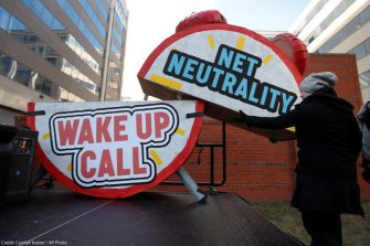 A person setting up a large sign that reads "WAKE UP CALL" and "NET NEUTRALITY" at a protest or rally.