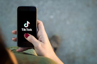 A person holding a smartphone displaying the TikTok logo on the screen.