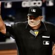 An MLB umpire signaling during a game, wearing a mask and an official uniform. An MLB umpire signaling during a game, wearing a mask and an official uniform.