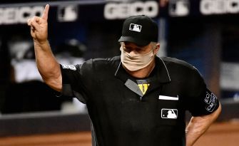 An MLB umpire signaling during a game, wearing a mask and an official uniform.