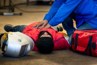 A construction worker receiving emergency assistance on the ground, with safety gear and a medical kit nearby.
