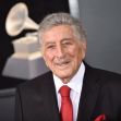 Tony Bennett smiling at an event, dressed in a black suit with a red tie. Tony Bennett smiling at an event, dressed in a black suit with a red tie.