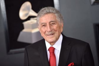 Tony Bennett smiling at an event, dressed in a black suit with a red tie.
