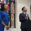 A press conference featuring two speakers, one in a blue dress and the other in a suit, standing at a podium with stained glass windows in the background. A press conference featuring two speakers, one in a blue dress and the other in a suit, standing at a podium with stained glass windows in the background.