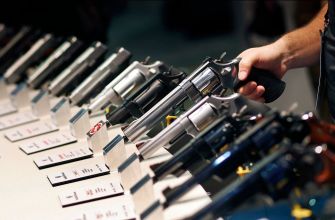 A display of various handguns on a table, with a hand holding one revolver.