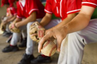 A baseball player holding a ball while seated on a bench during a game.