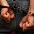 A person in handcuffs with their hands clasped behind their back, wearing jeans. A person in handcuffs with their hands clasped behind their back, wearing jeans.