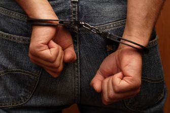 A person in handcuffs with their hands clasped behind their back, wearing jeans.
