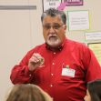 A man in a red shirt is speaking to a group of students in a classroom setting. A man in a red shirt is speaking to a group of students in a classroom setting.