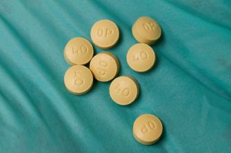Yellow opioid pills scattered on a teal surface.