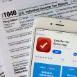 Image of a smartphone displaying the TurboTax app alongside IRS tax forms, specifically the 1040 Individual Income Tax Return. Image of a smartphone displaying the TurboTax app alongside IRS tax forms, specifically the 1040 Individual Income Tax Return.