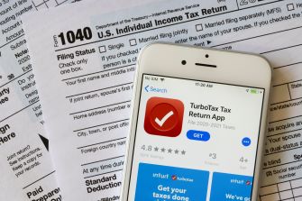Image of a smartphone displaying the TurboTax app alongside IRS tax forms, specifically the 1040 Individual Income Tax Return.
