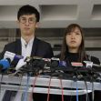 A young man and woman stand at a podium surrounded by microphones, likely preparing to address the media regarding political issues in Hong Kong. A young man and woman stand at a podium surrounded by microphones, likely preparing to address the media regarding political issues in Hong Kong.