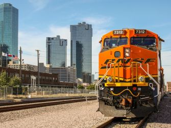 A BNSF Railway train in an urban setting with high-rise buildings in the background.