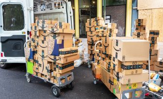 Stacks of Amazon packages on carts beside a delivery van.
