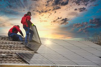 Workers installing solar panels on a roof at sunset.