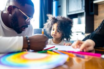 A child coloring with a parent at a table, surrounded by crayons and drawings.